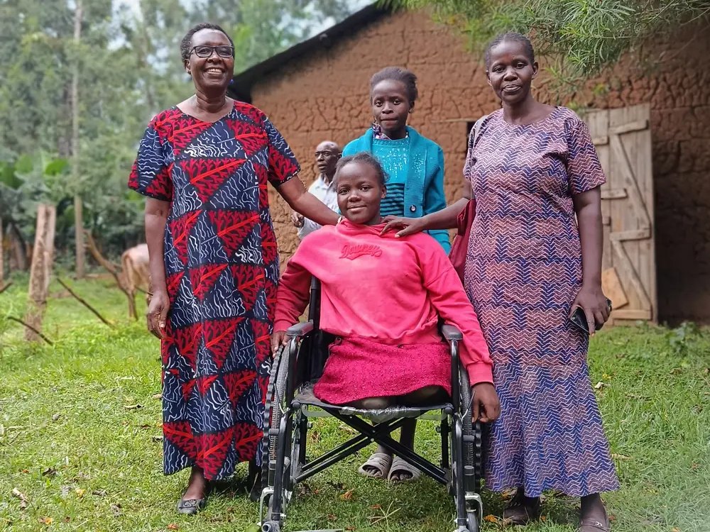 Smiling young woman in her new wheelchair with Destiny Impact members, Bungoma County, 2025